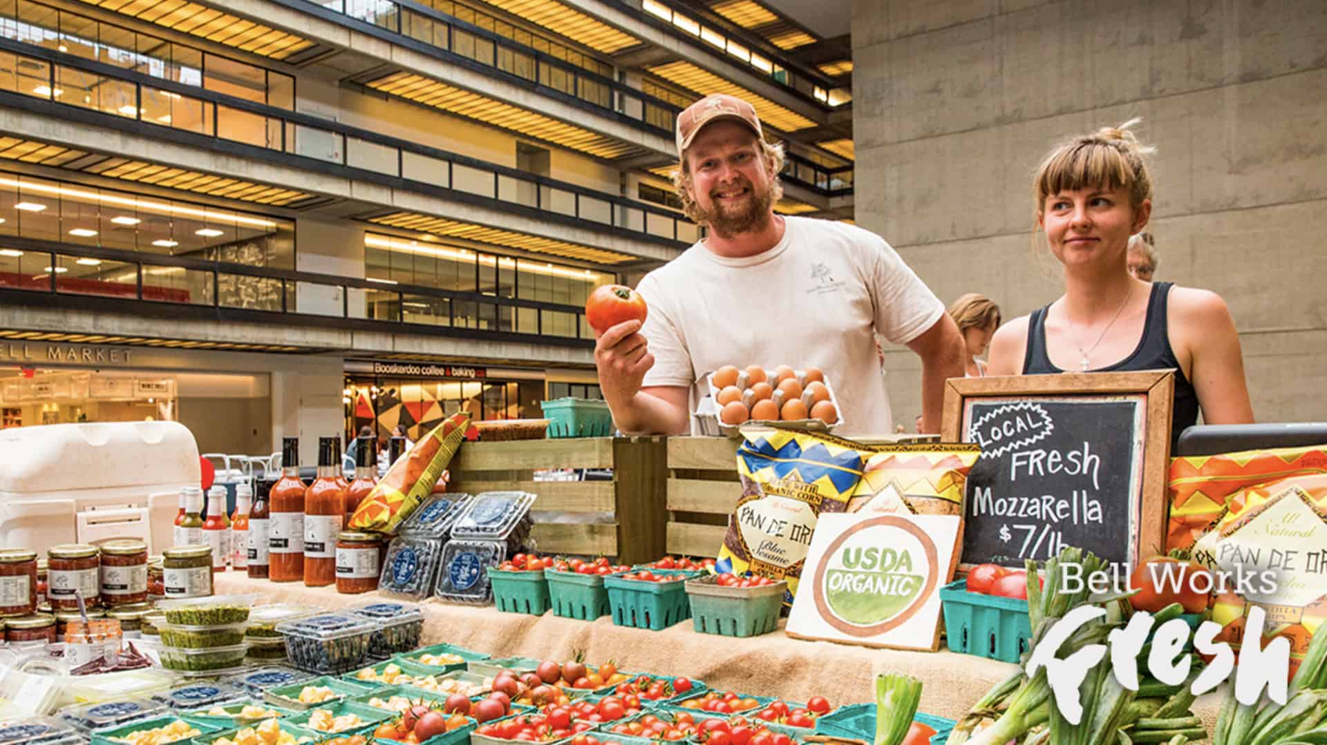 a couple buys produce at a farmers market and the Bell Works Fresh logo is on display in the bottom right-hand corner