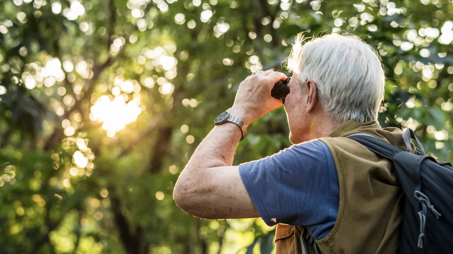 an elderly man watching birds with binoculars