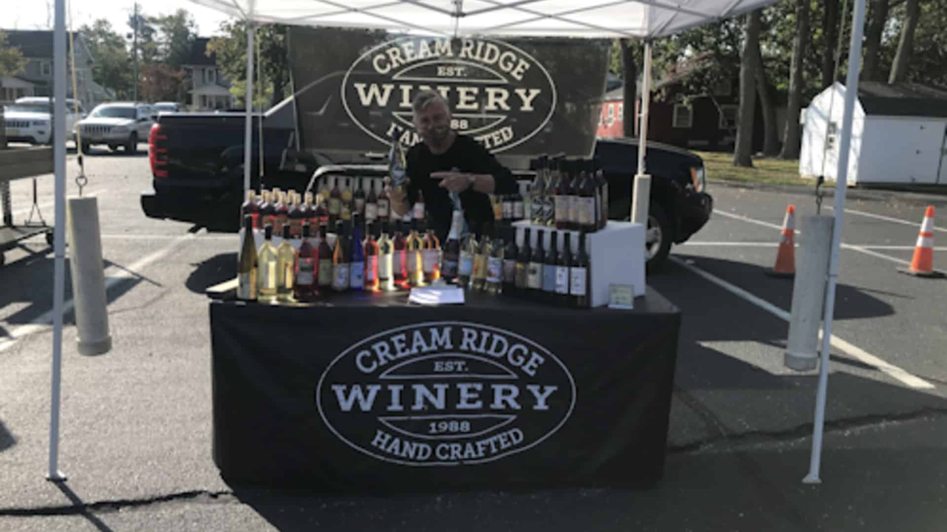 a man sells wine at an outdoor table for Cream Ridge Winery