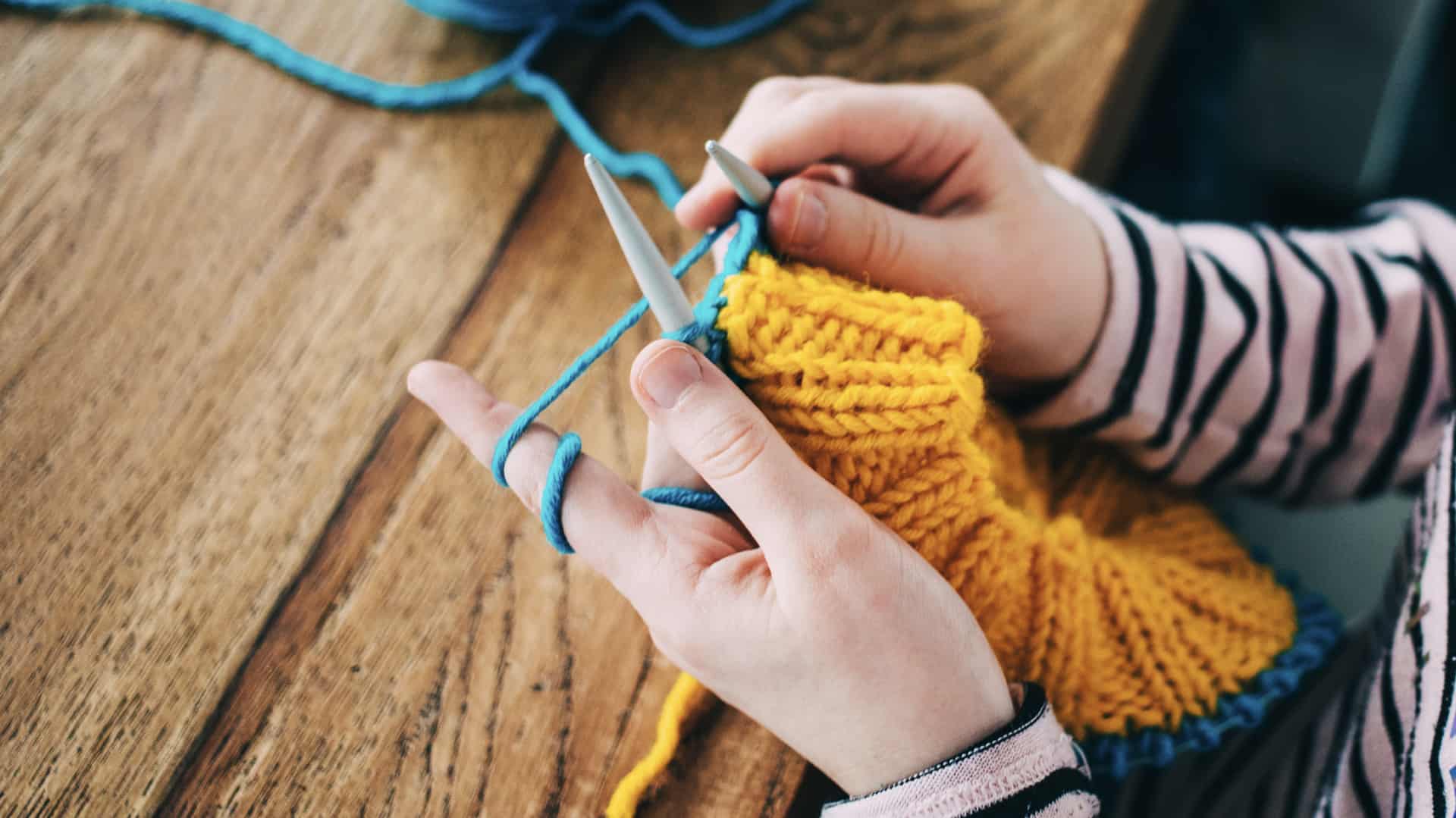 a young girl knitting a circle scarf with yellow and blue colored yarn