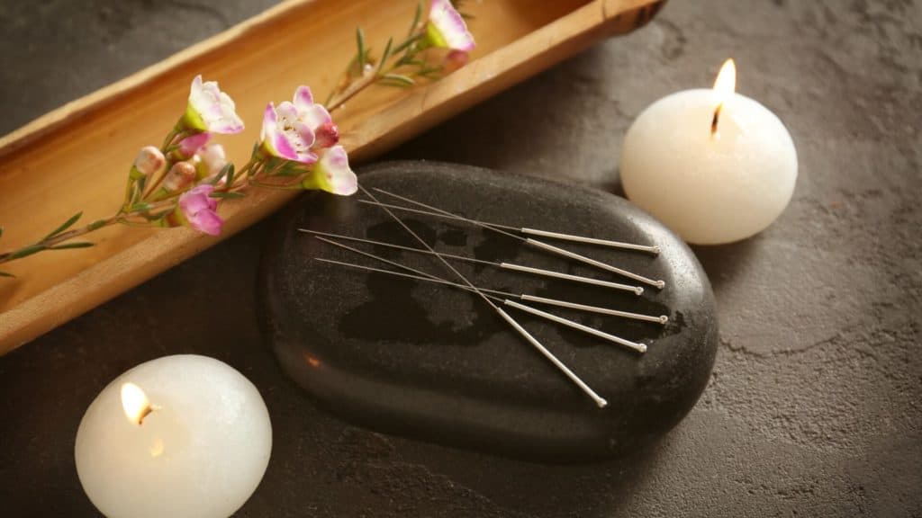 acupuncture needles sit with stone and candles on a textured background
