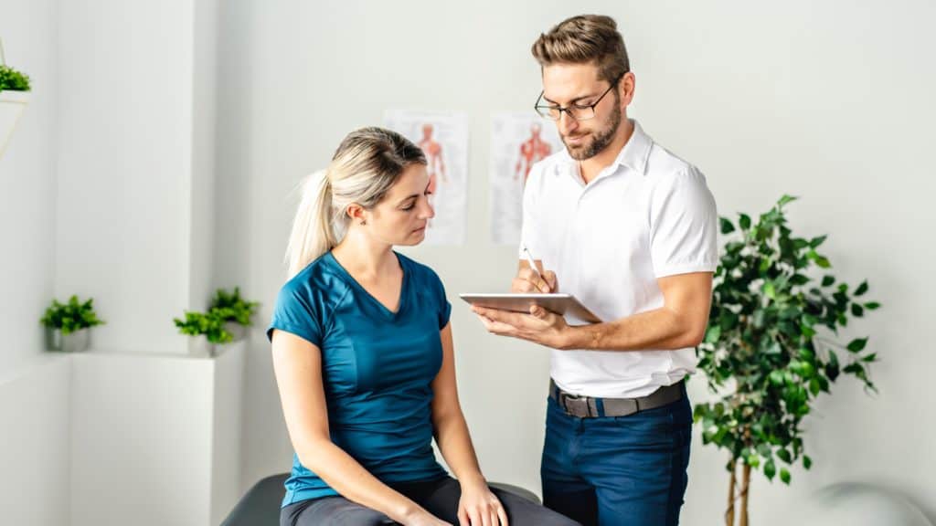 a chiropractor takes notes with their patient