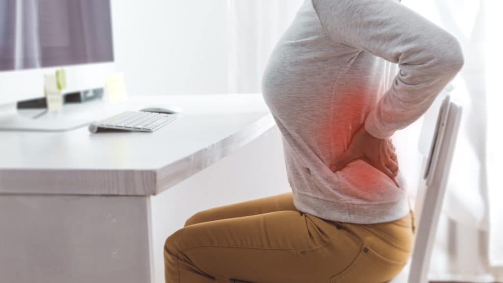 a person grips back in pain while sitting at their desk