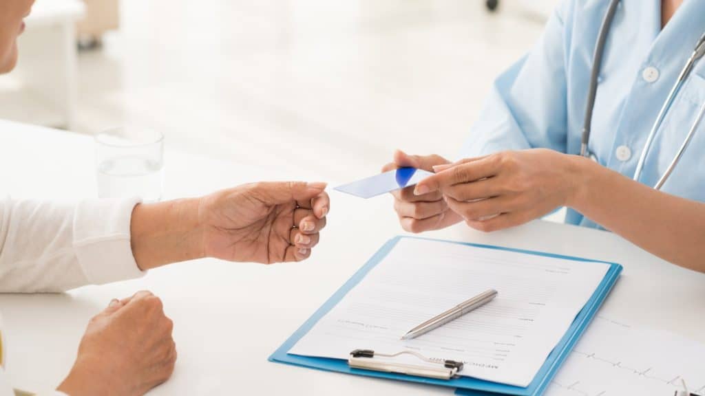 Patient hands a medical insurance card to a doctor | Frequently Asked Questions About Migraines | NorthEast Spine and Sports Medicine