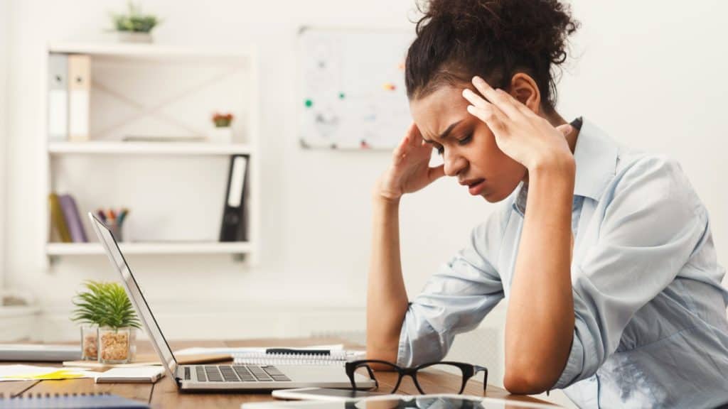 a woman has a headache while sitting at her work desk | Types of Headaches | NorthEast Spine and Sports Medicine