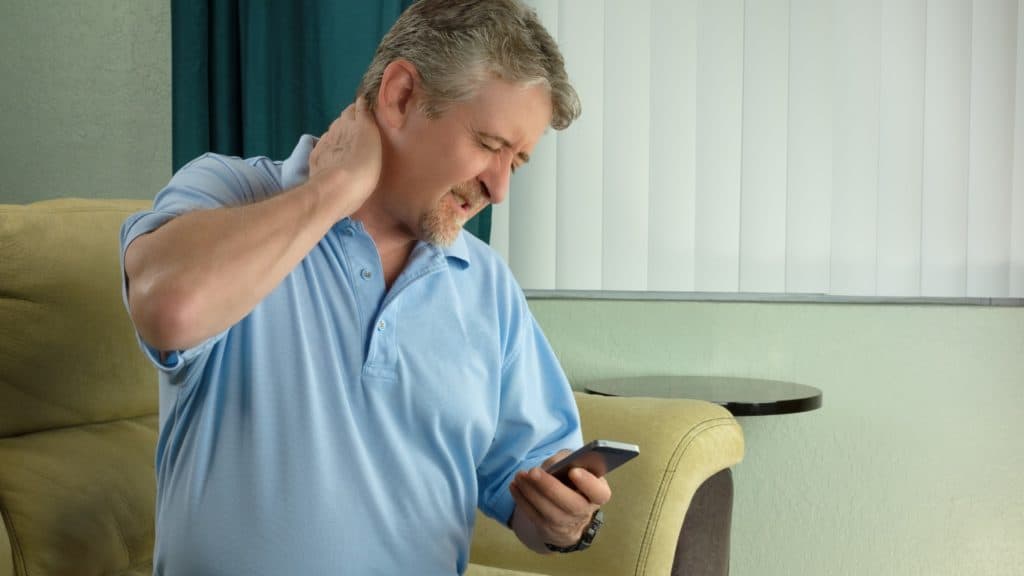 Man holding neck in pain while looking at phone | What Is Tech Neck? | Northeast Spine and Sports Medicine