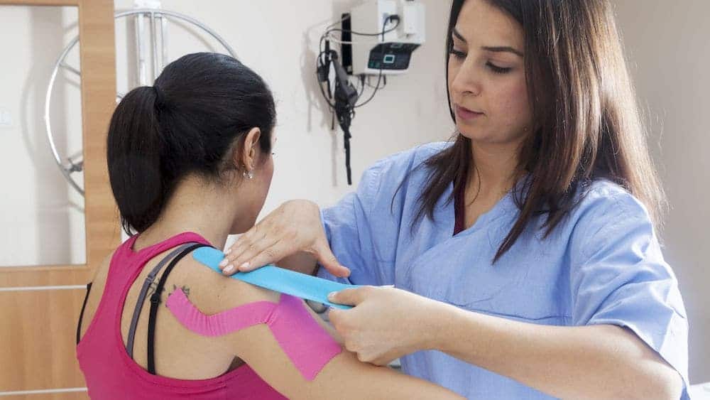 Female sports medicine physician puts athletic tape on patient's shoulder | Northeast Spine and Sports Medicine