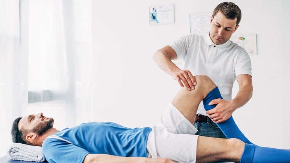 Sports medicine physician stretches athletes leg while laying on table | Northeast Spine and Sports Medicine