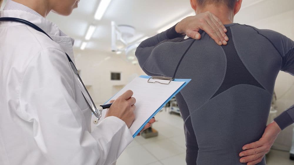 Sports medicine physician writes on clipboard while patient complains of back pain | Northeast Spine and Sports Medicine