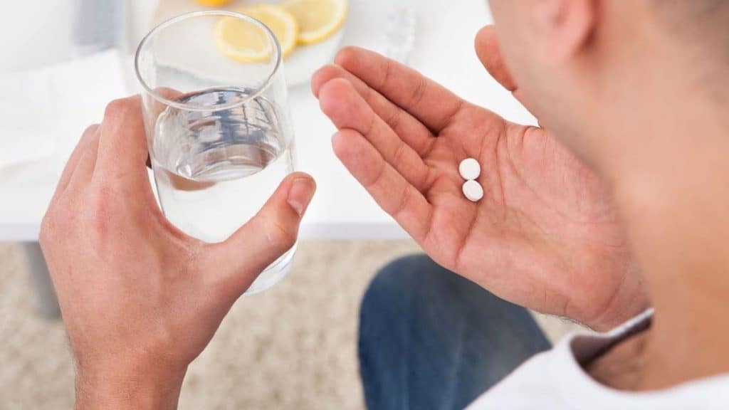 Close up of person holding glass of water and two white pills | NorthEast Spine and Sports Medicine