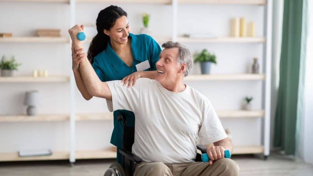 Physical therapist extends elderly man's shoulder in wheelchair | NorthEast Spine and Sports Medicine