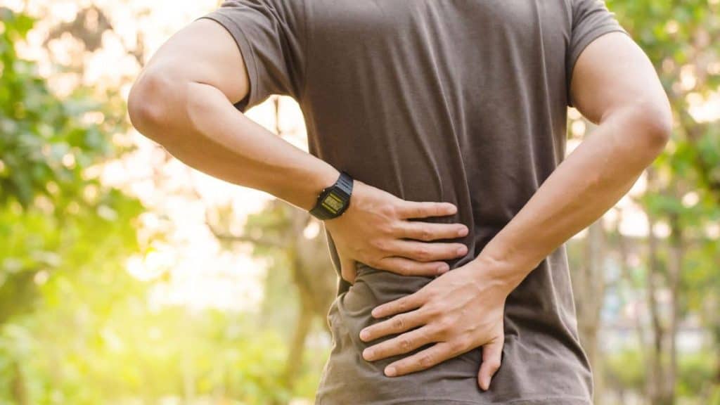 Man holding his lower back in pain while outdoors | NorthEast Spine and Sports Medicine