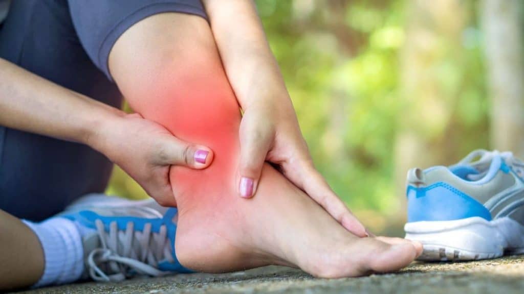 Sitting person holding their red, swelling ankle in pain | NorthEast Spine and Sports Medicine