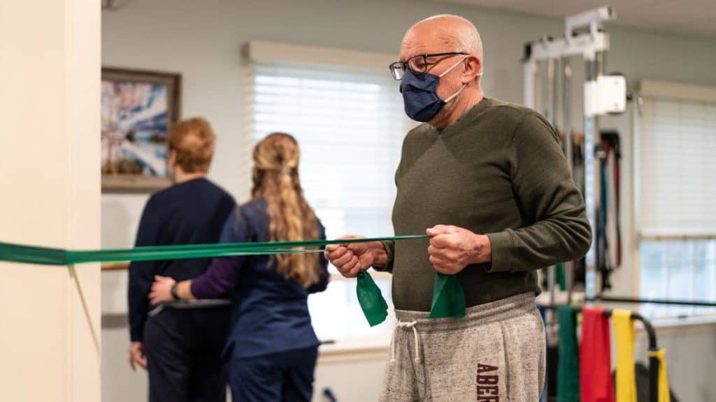 Physical therapist at NorthEast Spine and Sports Medicine helps elderly patients use elastic bands to test strength