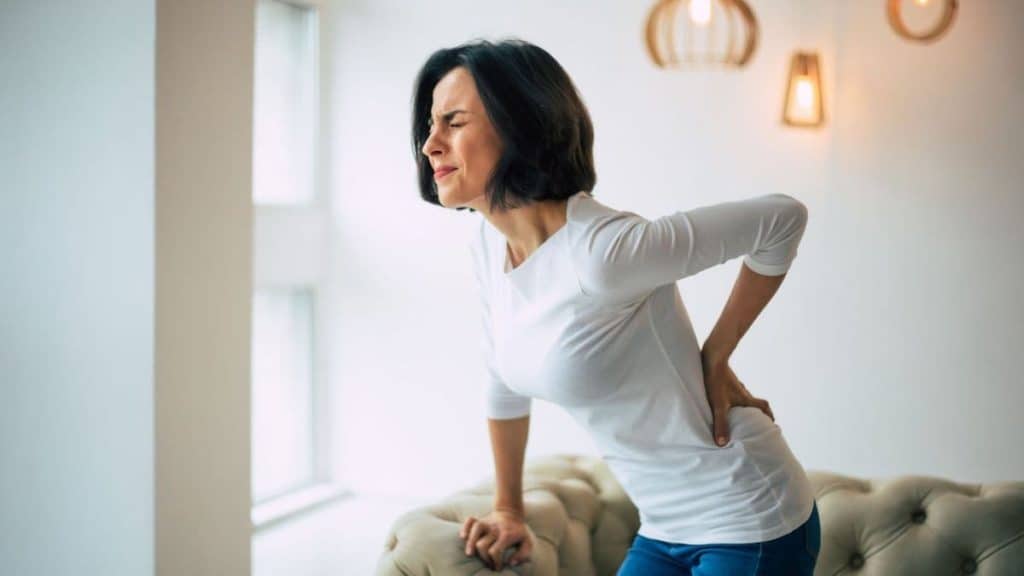 Woman bent over in pain while holding lower back | Acupuncture for Back Pain at Northeast Spine and Sports Medicine