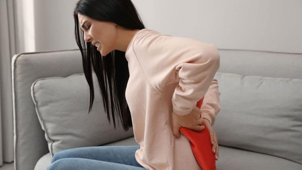 Woman in pain places heating pad on back | Back Pain Treatment at Northeast Spine and Sports Medicine