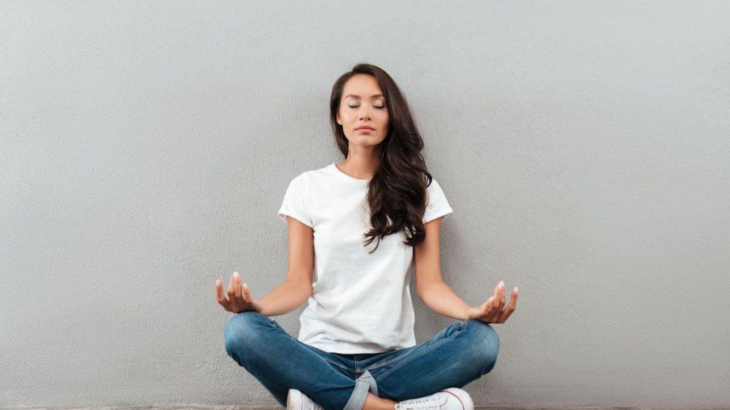 Woman meditating against gray wall | Back Pain Treatment at Northeast Spine and Sports Medicine