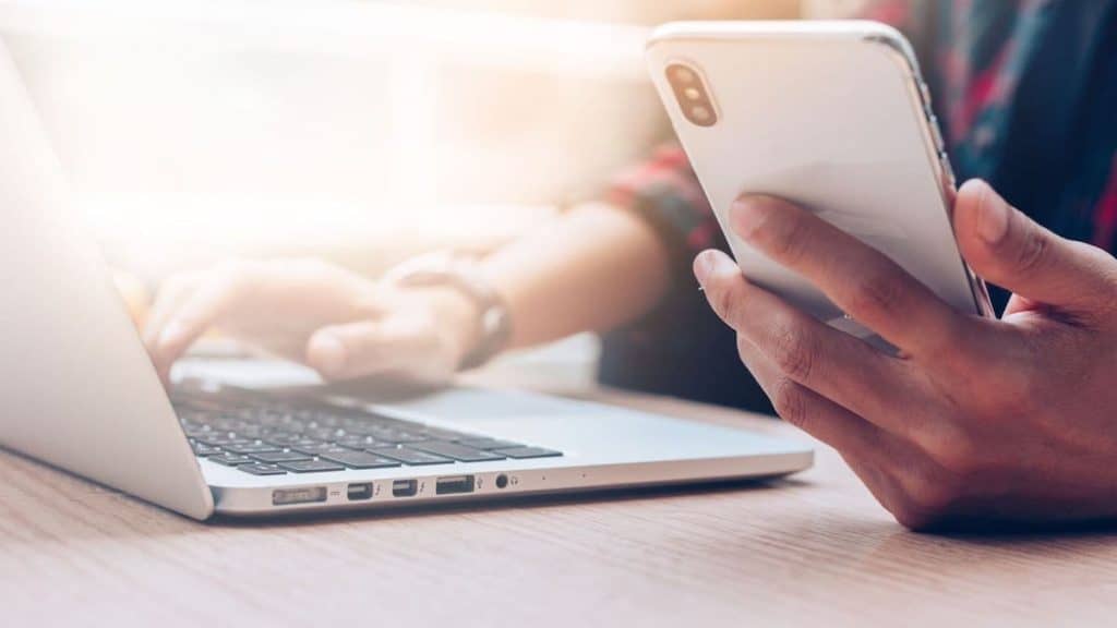 Close up of person's hand holding smartphone near laptop | Acupuncture for Back Pain at Northeast Spine and Sports Medicine