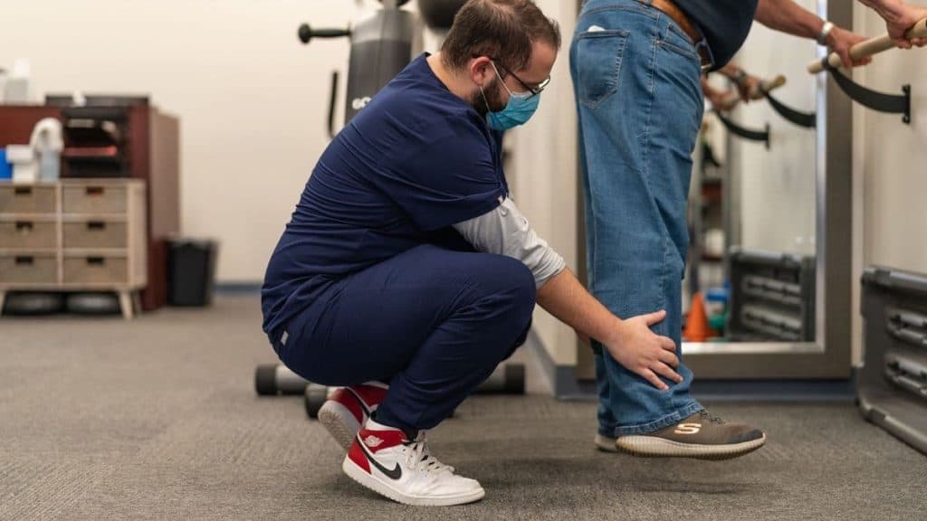 Physical therapist at NorthEast Spine and Sports Medicine holds patient's ankle as they conduct balance training