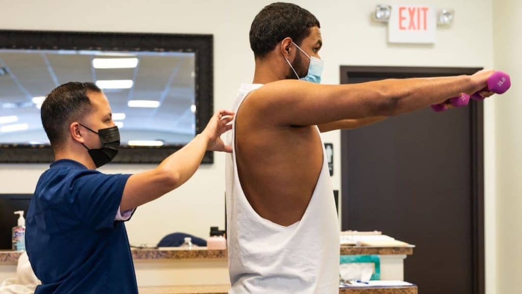 Physical therapist at NorthEast Spine and Sports Medicine helps man raise weights in strength exercise