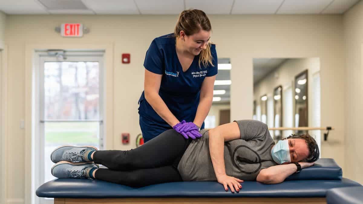 Physical therapist at NorthEast Spine and Sports Medicine presses female patient's hip while laying on table during session