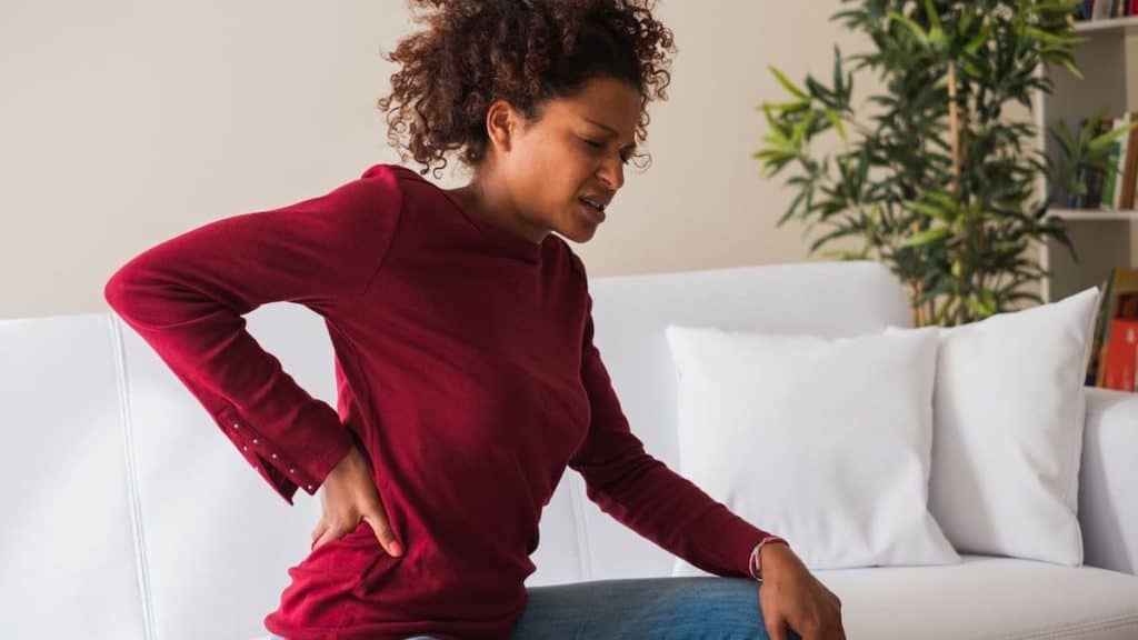 Stressed woman reached for her lower back in pain | Northeast Spine and Sports Medicine
