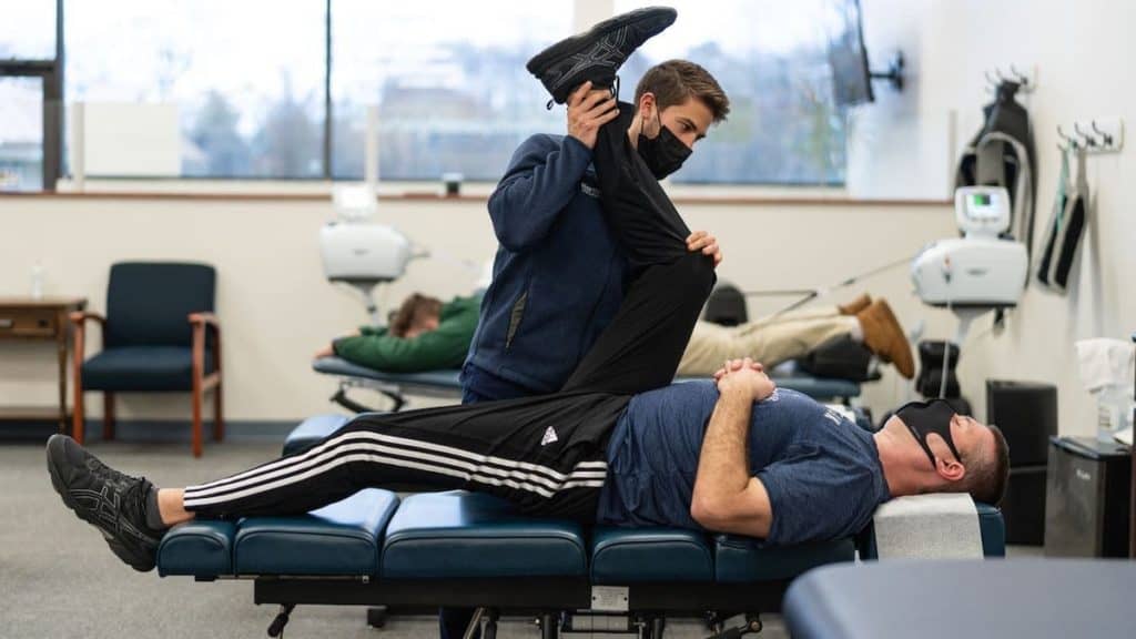 Patient lays on exam table while chiropractor helps life his leg towards his head | Northeast Spine and Sports Medicine