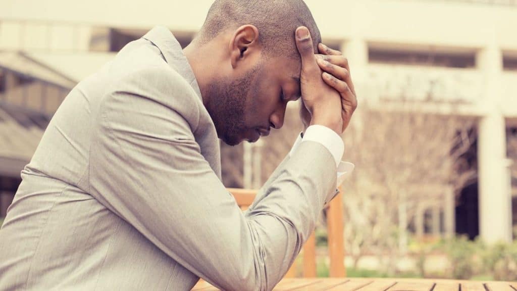 Stressed man leans against fence while holding his head in pain | Northeast Spine and Sports Medicine