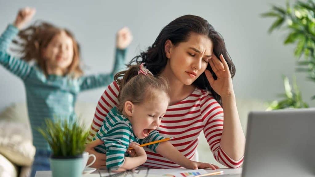 Mother grabs her head in pain while holding her child in her lap at table | Northeast Spine and Sports Medicine