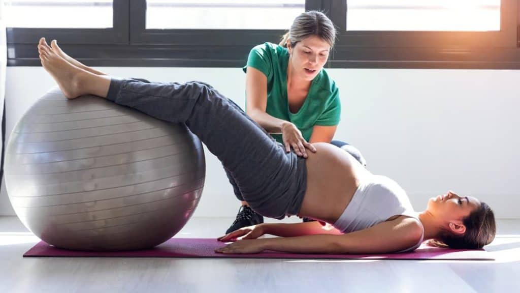 Pregnant patient stretching her hips with the help of a physical therapist | NorthEast Spine and Sports Medicine